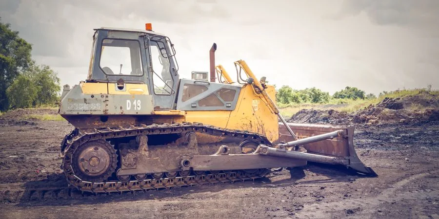 Powerful bulldozer on muddy construction ground — rubber tracks distributing machine weight across soft terrain, the same principle that makes mini dump trucks on tracks effective on soft clay, wet grass, and sloped sites
