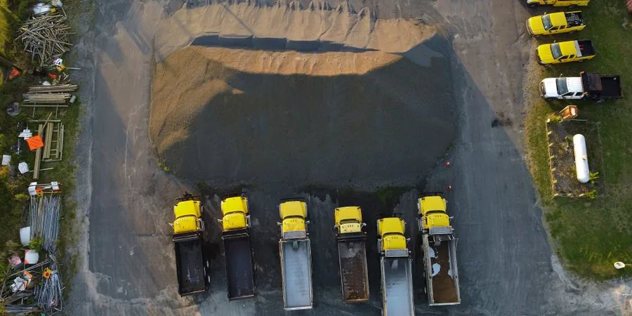 Aerial view of yellow trucks aligned by a gravel heap at an industrial site — the scale of material handling at a large operation, contrasted with the confined-access small dumper truck application