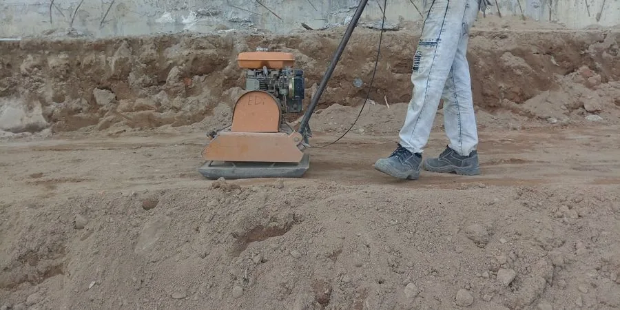Construction worker operating compact equipment outdoors on site — correct operation of small tracked machinery on uneven ground requires consistent technique on slopes and during the dump cycle