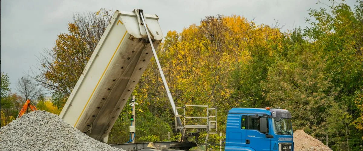 Blue dump truck unloading gravel at a construction site — the same material-displacement task a 500 kg mini dump truck on tracks handles on tight residential and commercial sites where larger machines cannot access