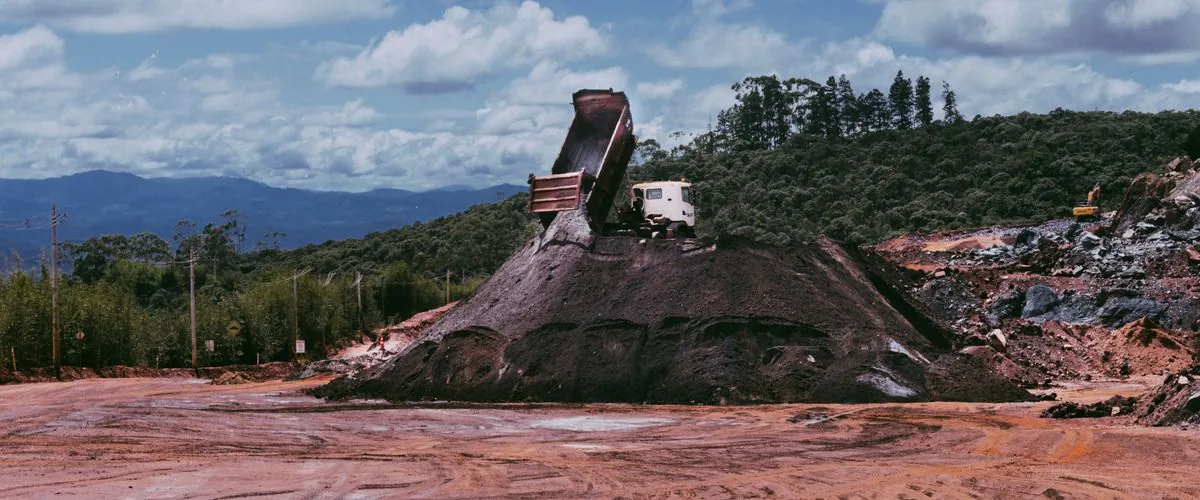 Dumper truck offloading soil at an open construction site under a blue sky