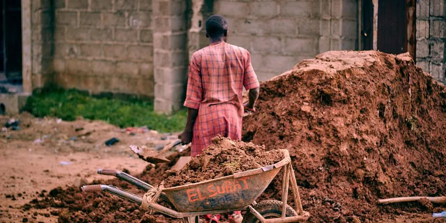 Construction worker moving soil with a traditional wheelbarrow on a site — the manual baseline that a mini track dumper replaces at 5–10 times the speed