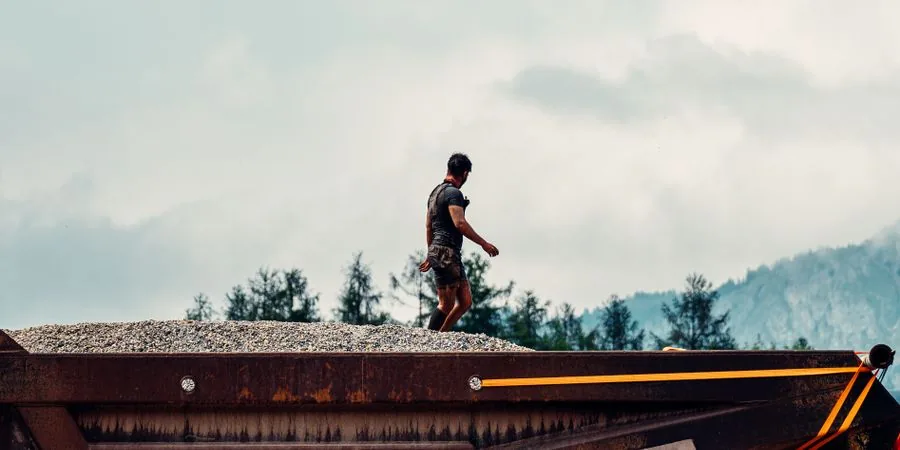 Construction worker standing on a gravel and rock heap at a site — terrain that determines whether a power wheelbarrow or tracked dumper is the right tool
