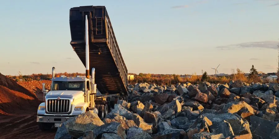 Dump truck unloading rocks at a quarry construction site at sunset — illustrating material discharge, the core function shared by mini dump trucks on tracks operating on residential and commercial sites