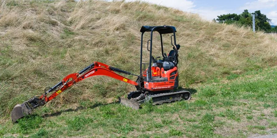 Red mini excavator on rubber tracks parked on a grassy hillside — illustrating the terrain capabilities shared by mini track dumpers on slopes and soft ground
