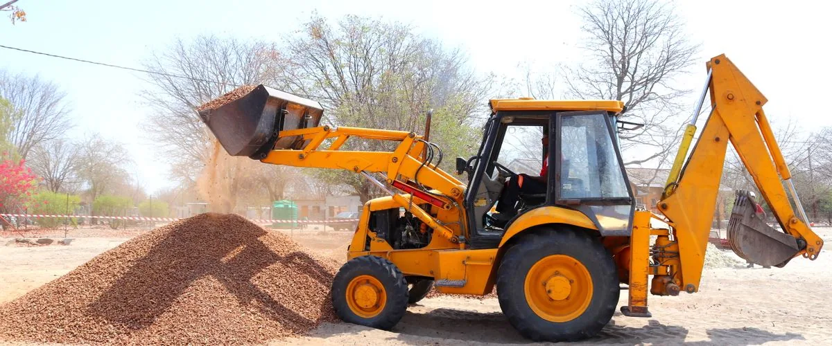 Yellow excavator moving gravel at an outdoor construction site — the earthmoving work that small dumper trucks support on restricted-access sites