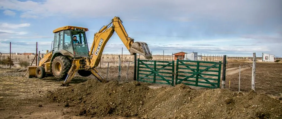 Yellow excavator at a farm entrance beside a green gate — illustrating the agricultural and narrow-access applications where self-loading mini tracked dumpers work without a second machine
