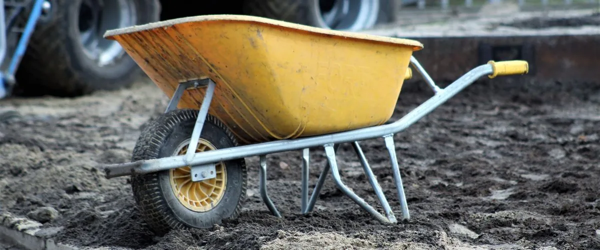 Yellow motorised power wheelbarrow on a construction site dirt ground — the entry-level machine for powered site material handling